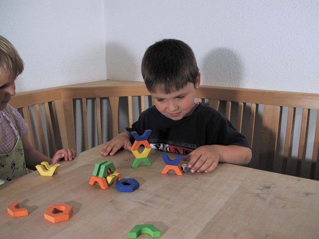 Junge spielt mit bunten Bhavátí-Holzteilen am Tisch